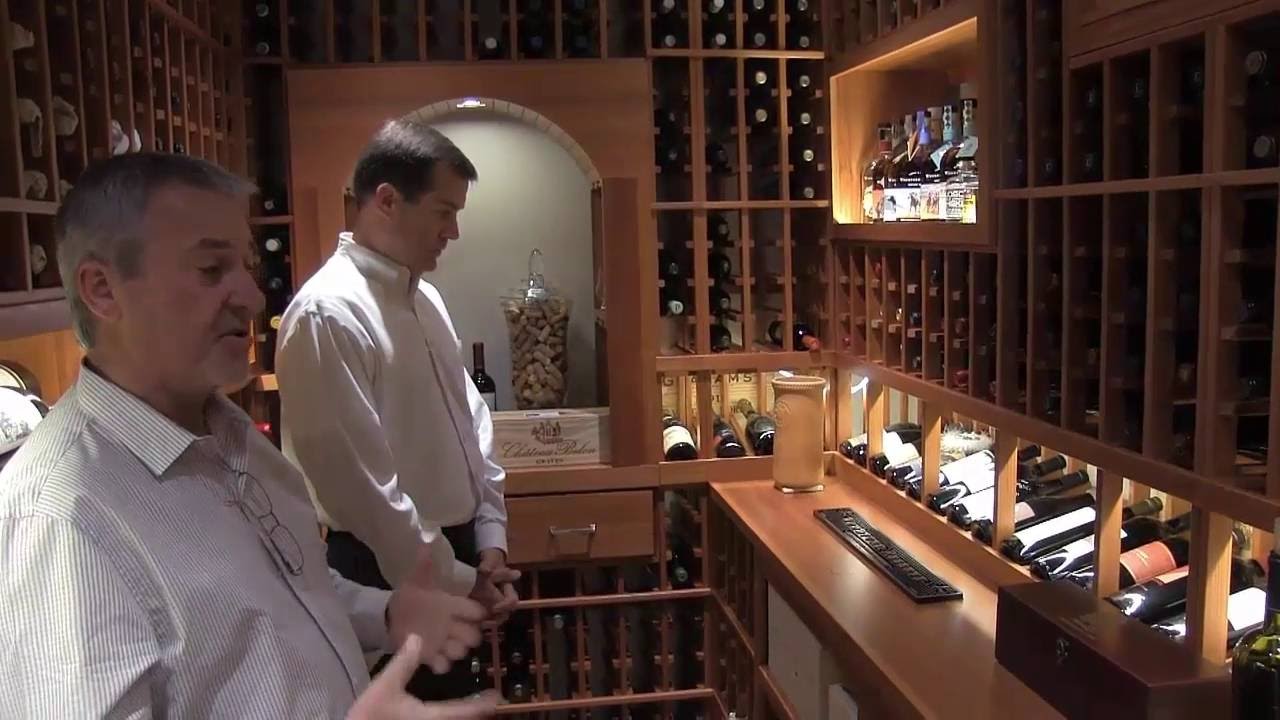 Two men in white shirts inside of a wine cellar, choose which wines they want.